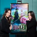 Myra Ruiz (Elphaba) e Fabi Bang (Glinda) ao lado do pôster do filme